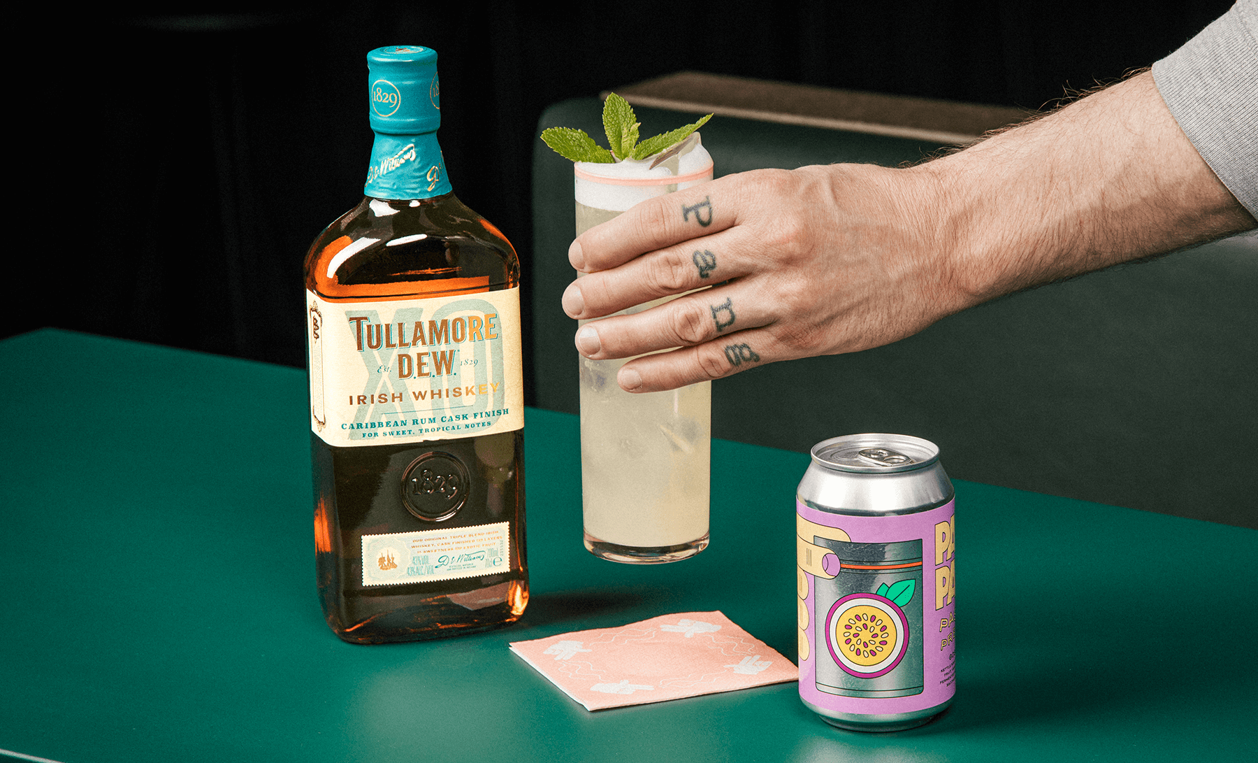 en drink en hand och en flaska på ett bord