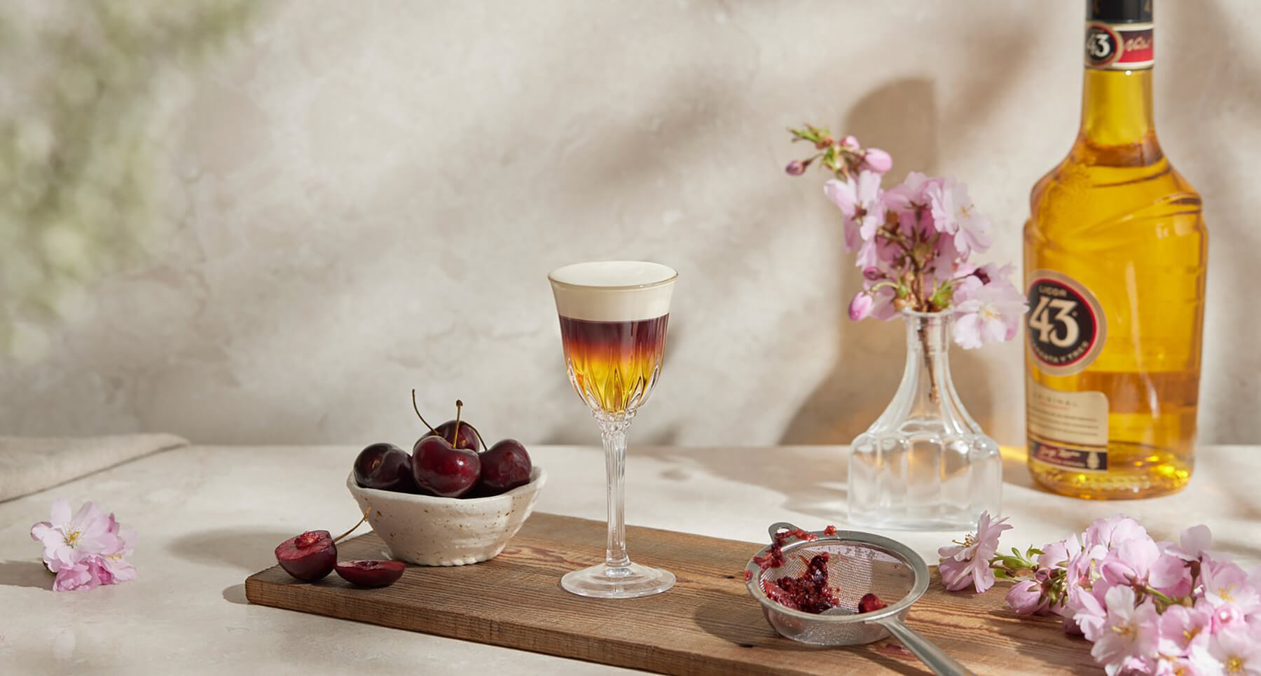 ett bord med shot glas och körsbär med en flaska licor 43